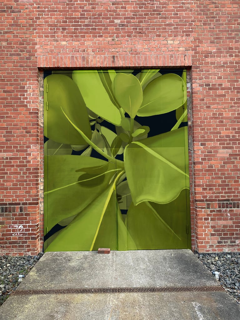 Doorway in red brick wall featuring large green tropical leaves filling the frame